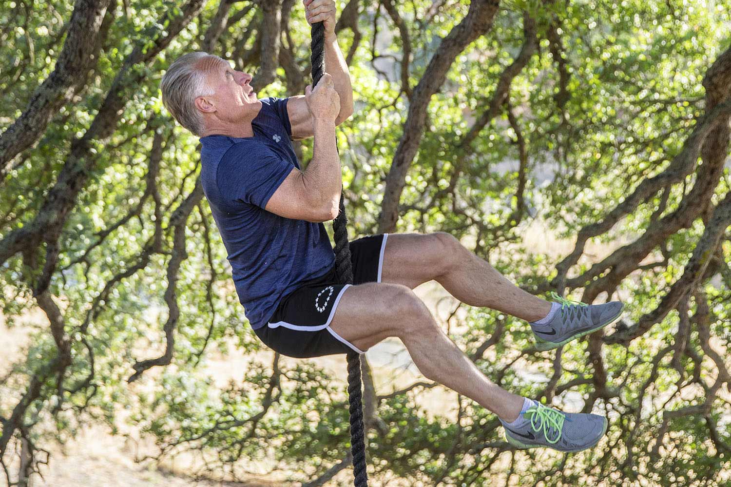 Dave climbs a rope beneath a large tree.